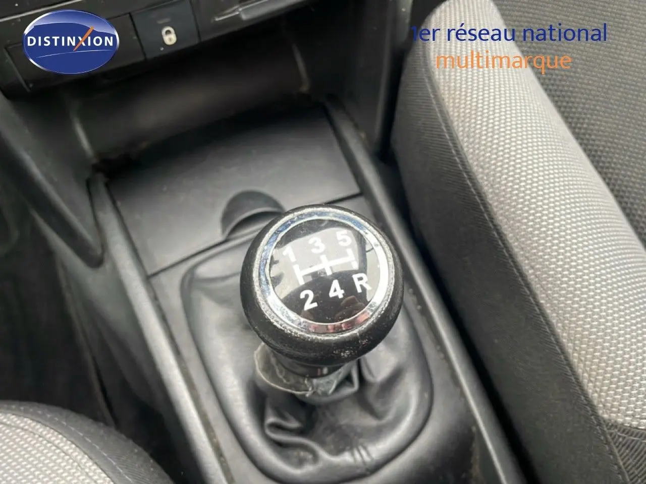 Le levier de vitesse manuel noir de la Peugeot 207 HDI 70CH TREND, entouré de sièges en tissu gris.