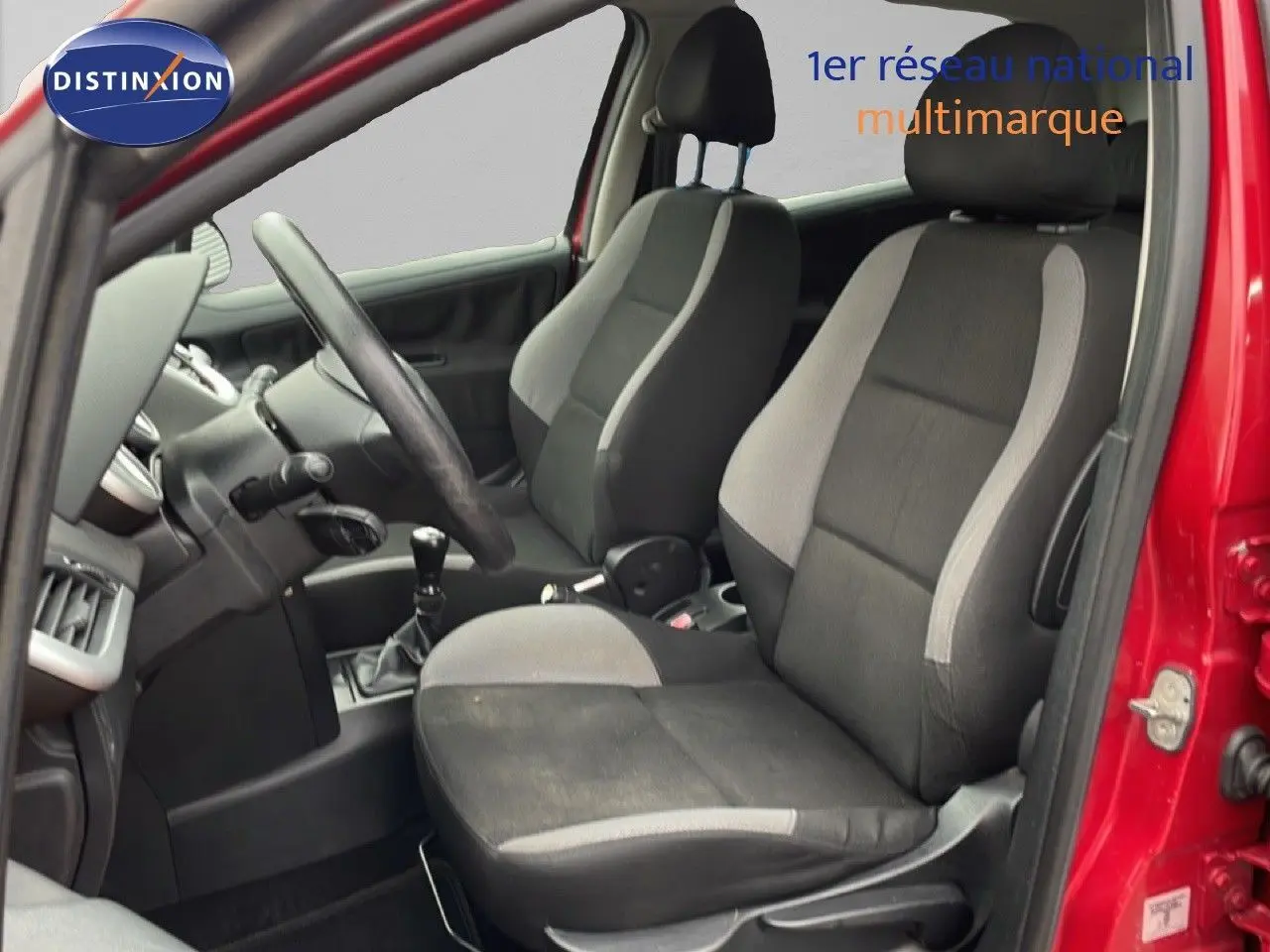 Intérieur de la Peugeot 207 rouge métal 2009, vue côté gauche, sièges tissu noir et gris avec levier de vitesse manuel.