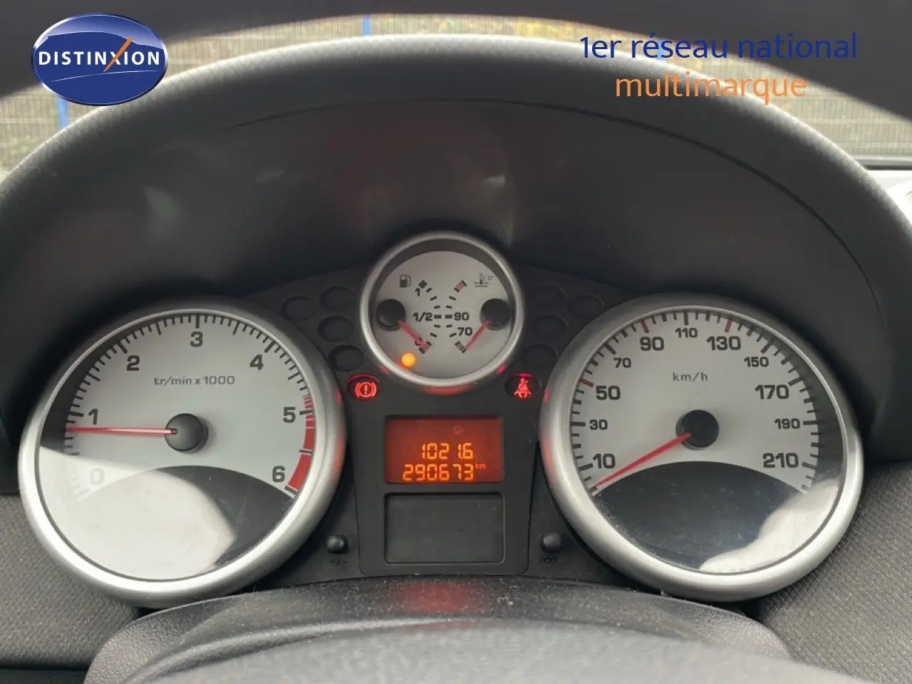 Vue rapprochée du tableau de bord de la Peugeot 207 rouge métal, montrant les compteurs et l'odomètre digital.