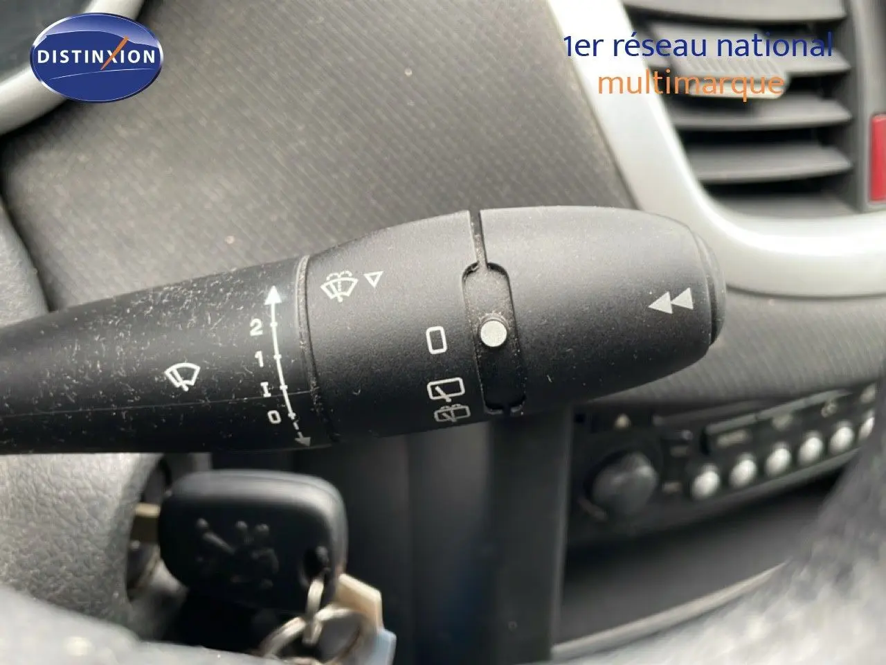 Gros plan sur la commande d’essuie-glace à gauche du volant dans l’habitacle d’une Peugeot 207 rouge métal de 2009.