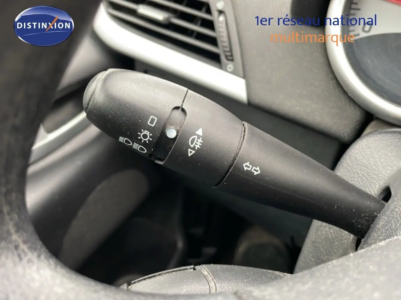 Gros plan sur la commande de clignotants à gauche du volant d'une Peugeot 207 rouge métal de 2009.