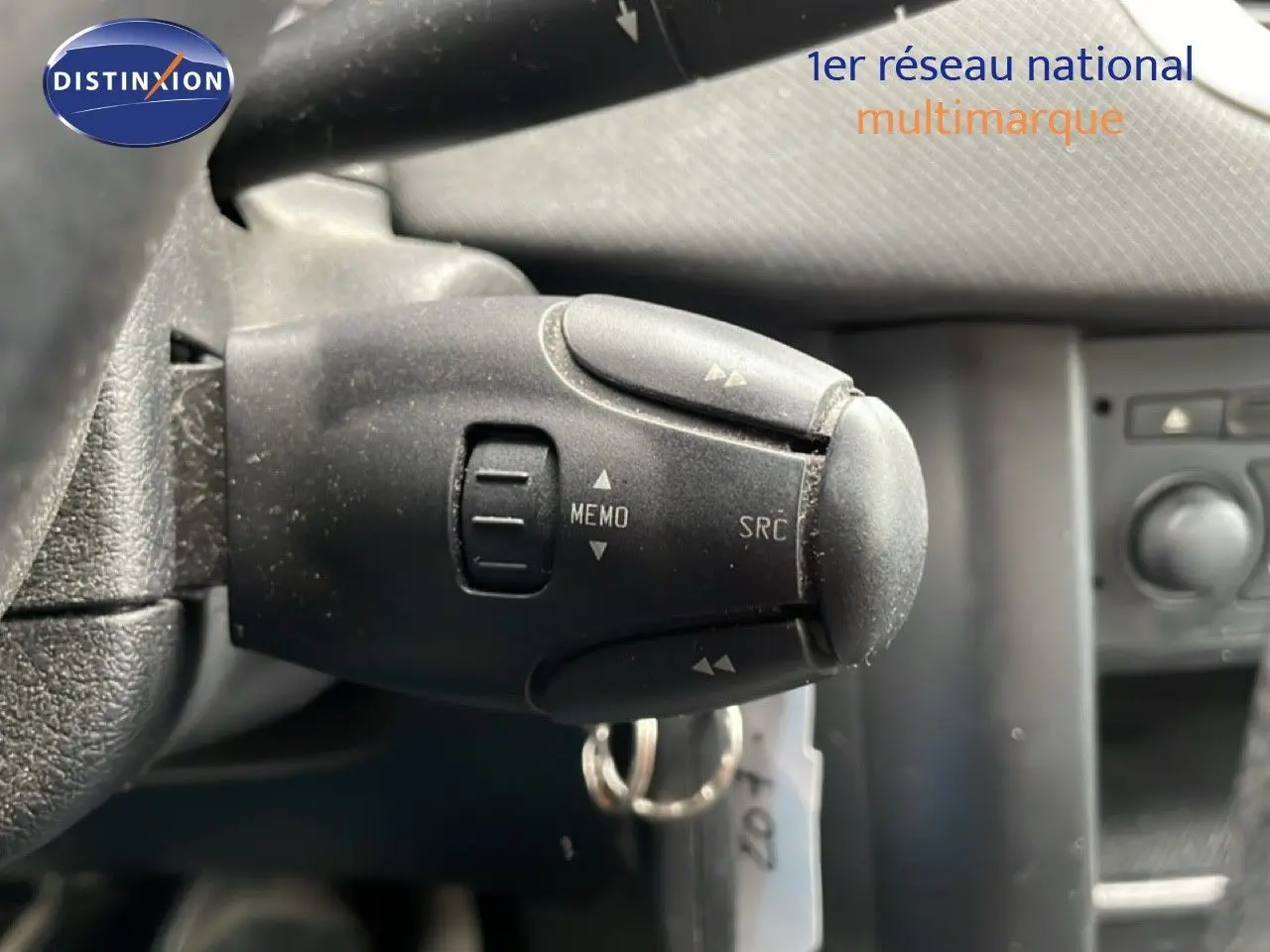 Gros plan sur la commande au volant de la Peugeot 207 rouge métal, montrant les boutons MEMO et SRC.