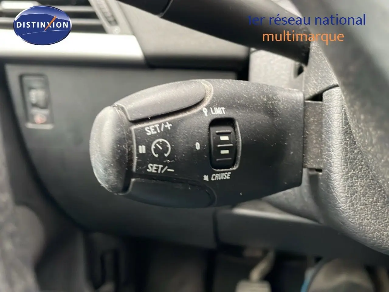 Gros plan sur la commande de régulateur de vitesse au volant d'une Peugeot 207 rouge métal de 2009.