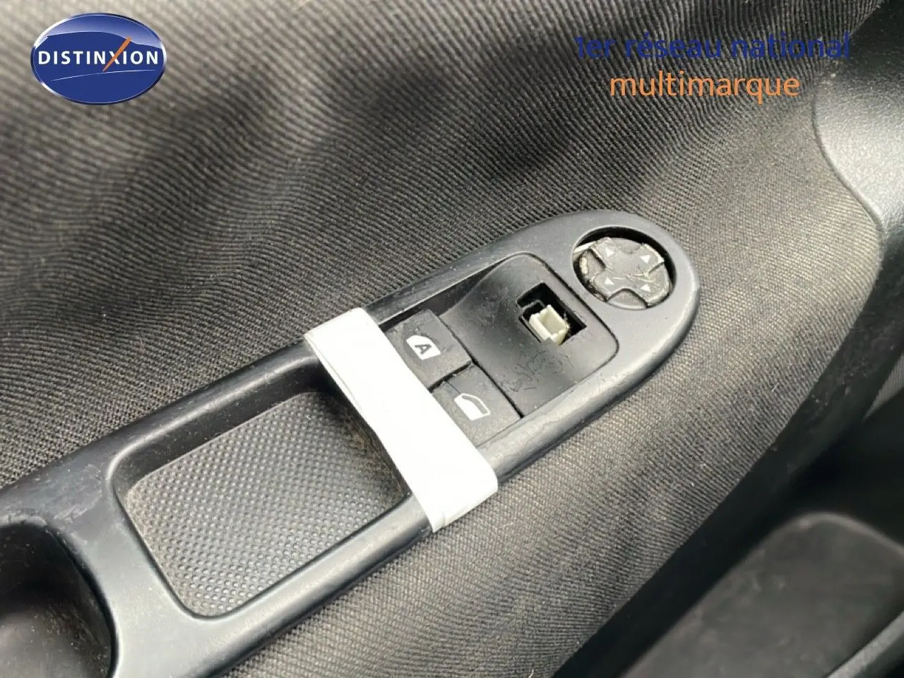 Gros plan sur les commandes de lève-vitres côté conducteur d'une Peugeot 207 rouge métal de 2009.