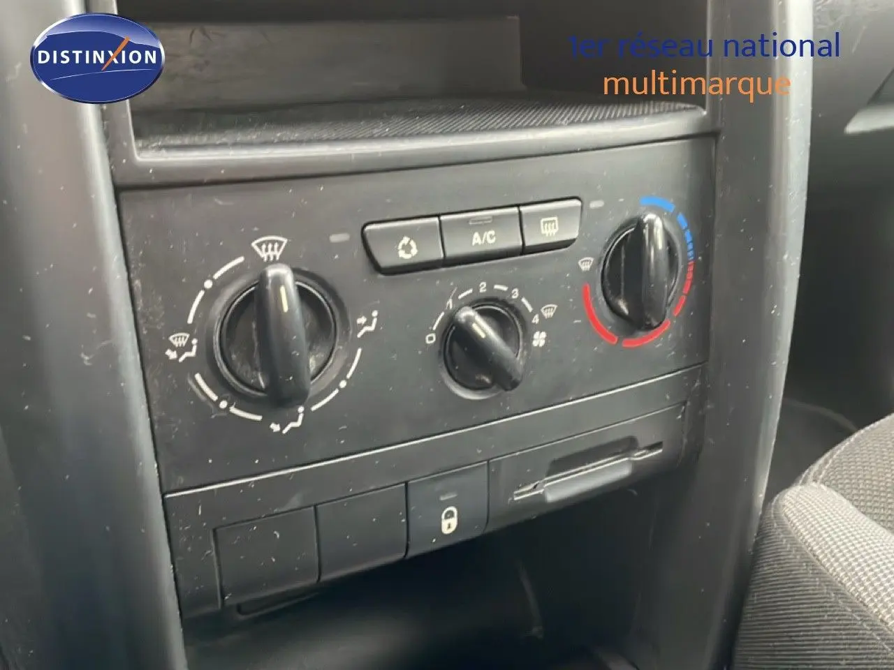 Gros plan sur la console centrale de la Peugeot 207 rouge métal, montrant les commandes de climatisation et ventilation.