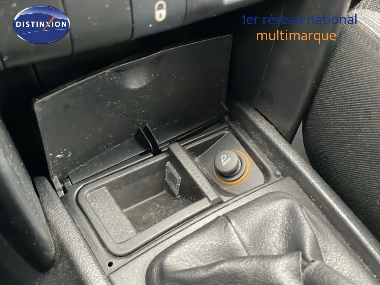 Gros plan sur la console centrale de la Peugeot 207 rouge métal, montrant l'allume-cigare et le soufflet de levier de vitesses.
