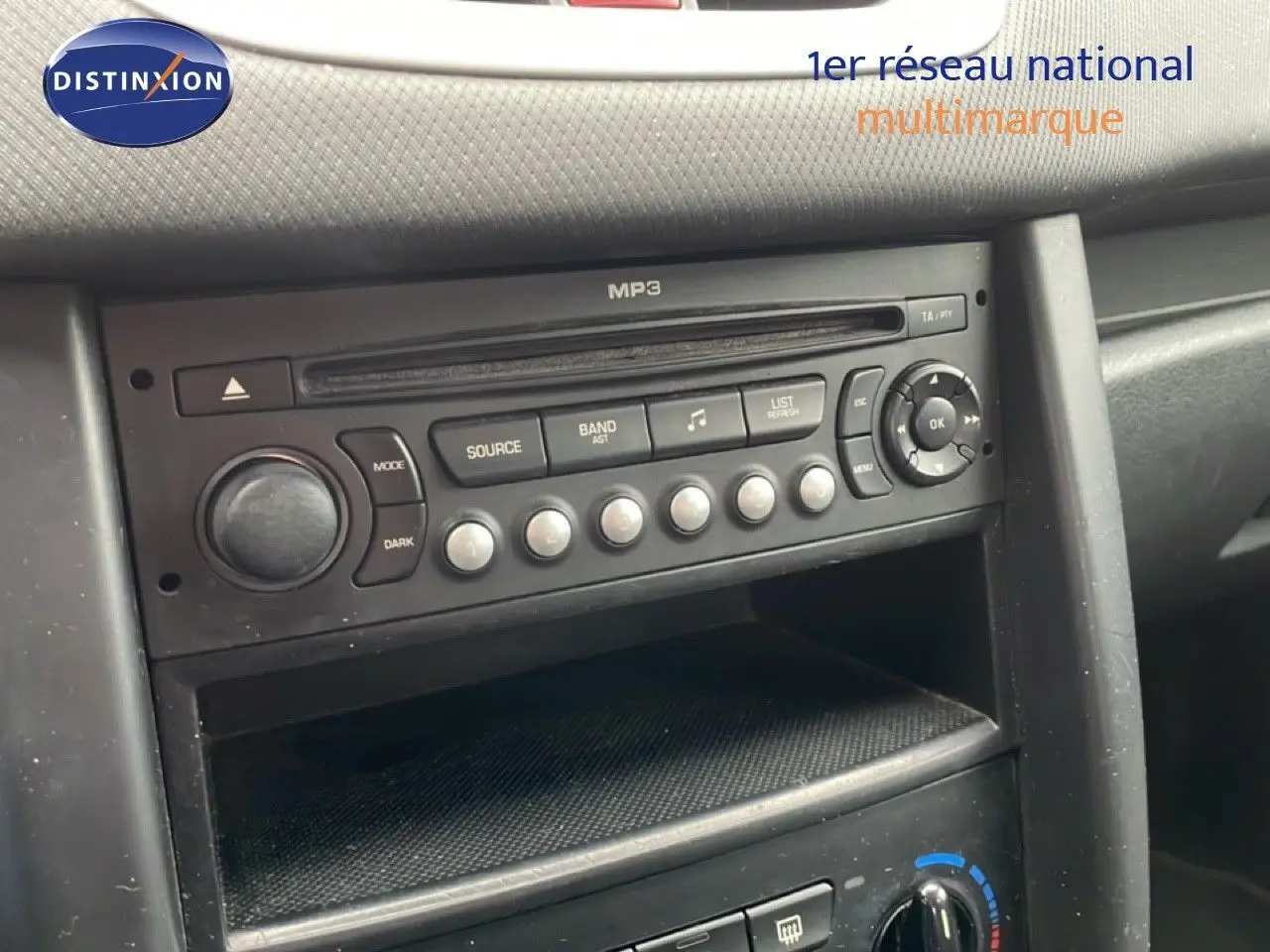 Vue rapprochée de la console centrale noire de la Peugeot 207 rouge métal, mettant en valeur la radio MP3 et les commandes climatiques.