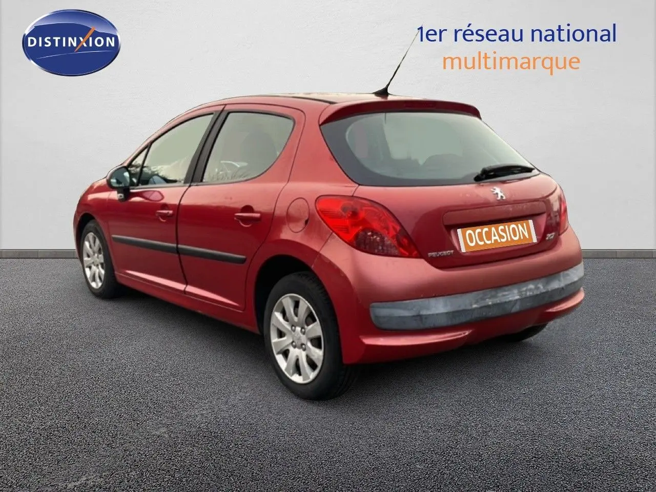 Vue 3/4 arrière droite d'une Peugeot 207 rouge métal cinq portes, avec plaques d'occasion visibles.