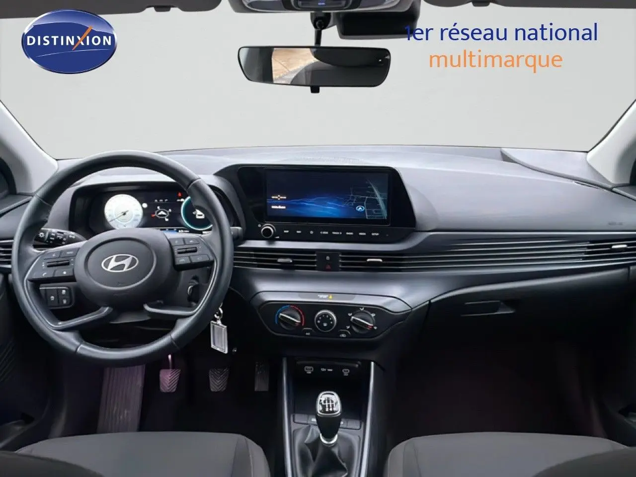 Vue intérieure avant du tableau de bord et volant de la Hyundai i20 2025 avec écran tactile et boîte manuelle.
