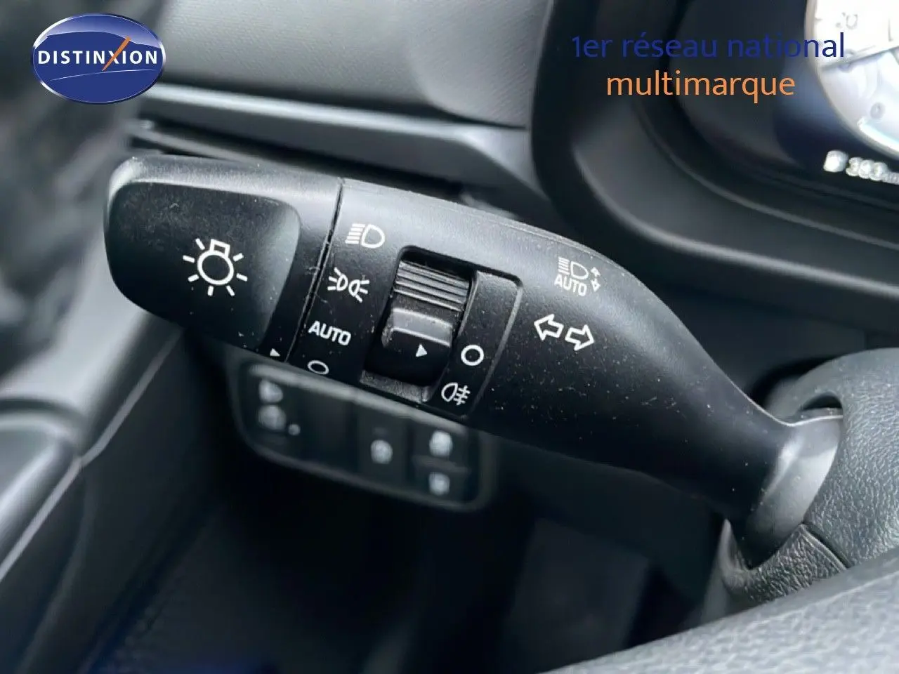 Gros plan sur la commande des feux et clignotants à gauche du volant dans une Hyundai i20 rouge Dragon Metal 2025.