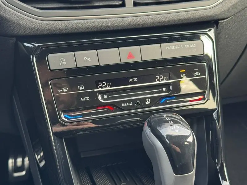 Gros plan sur la console centrale noire du Volkswagen T-Cross blanc, avec commandes climatisation digitale et levier de boîte automatique.
