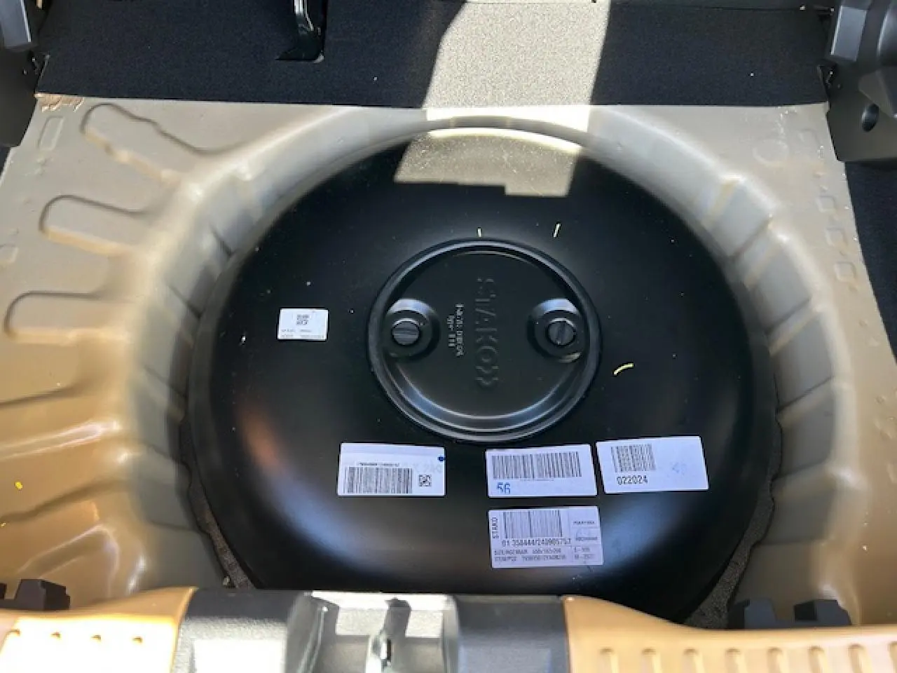 Vue plongeante sur le réservoir GPL noir dans le coffre beige Safari d'une Dacia Sandero III Stepway 2025.