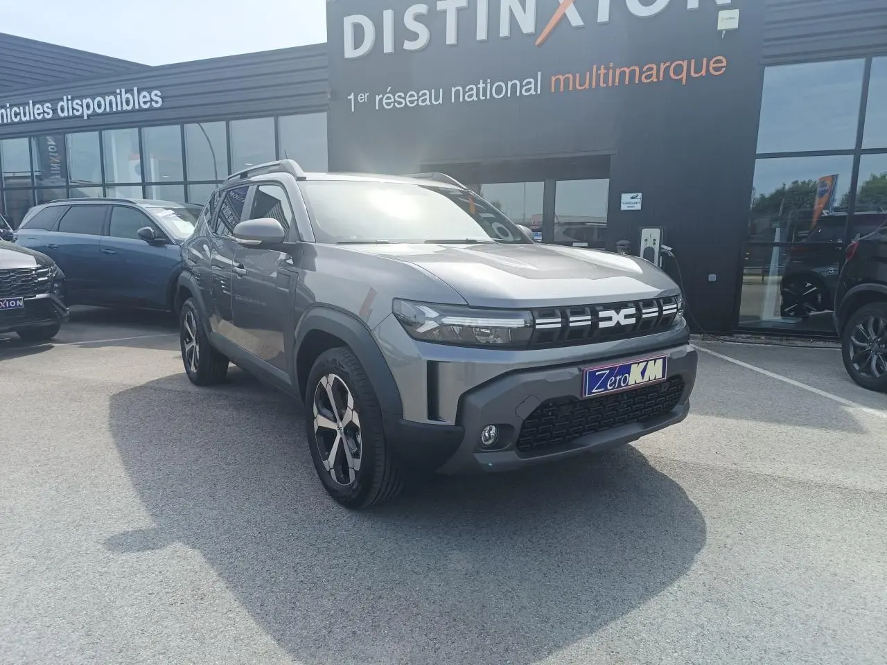 Vue 3/4 avant droit du Dacia Duster 2026 gris schiste métal avec jantes alliage et barres de toit noires.