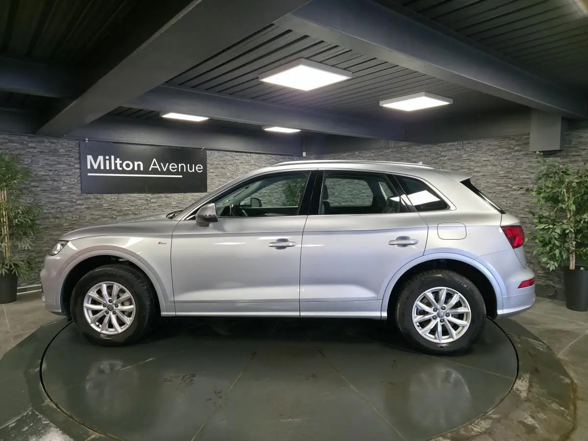 Audi Q5 gris en profil droit dans un showroom, avec jantes alliage et toit ouvrant visible.