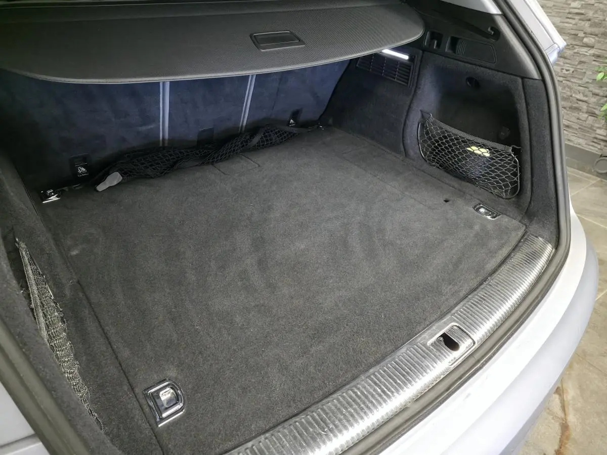Coffre ouvert vu de l'arrière d'un Audi Q5 gris, avec tapis de sol noir et filet de rangement latéral.