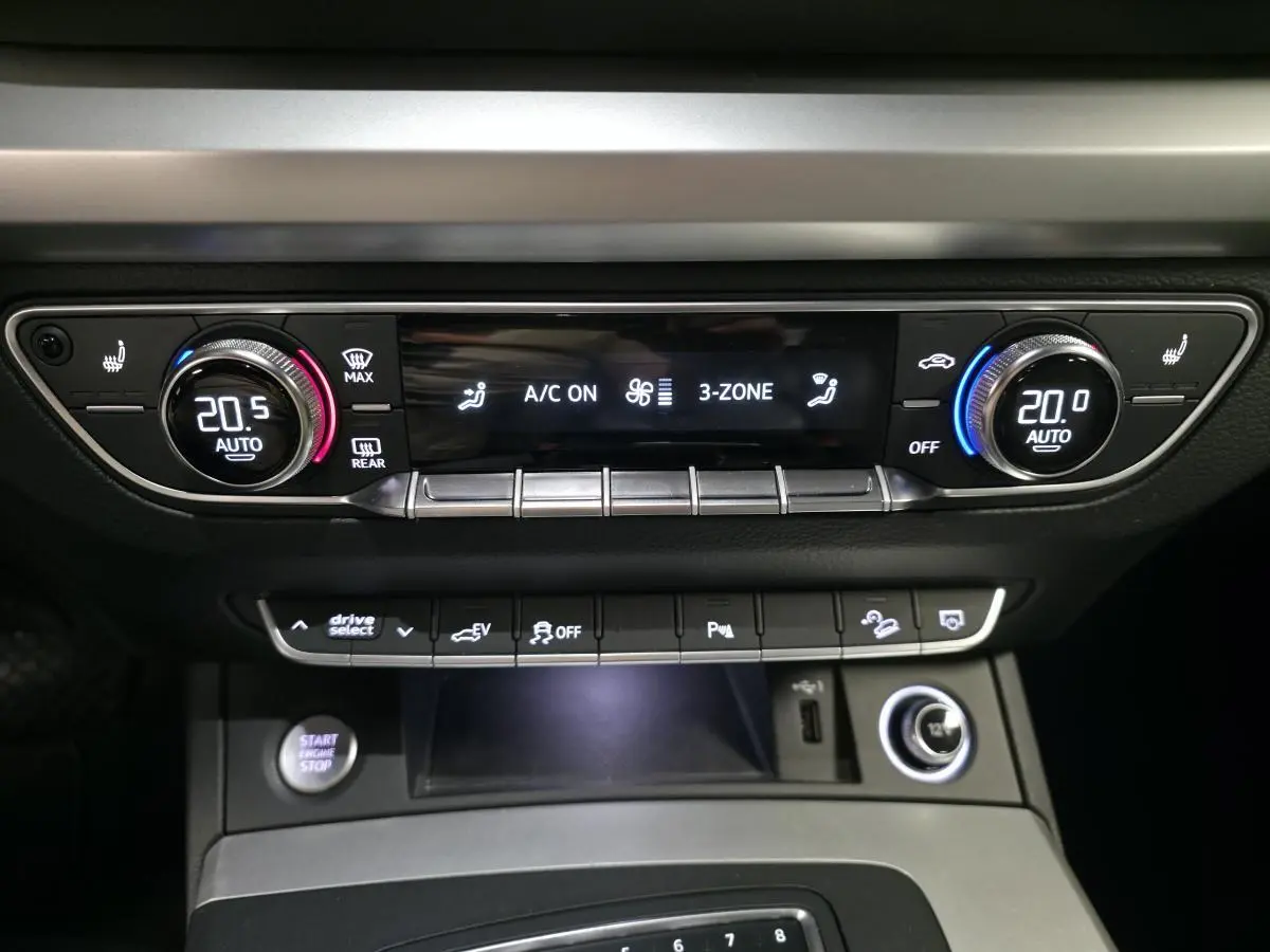 Tableau de bord de l'Audi Q5 gris, vue centrée sur la console de climatisation automatique 3 zones avec commandes digitales.