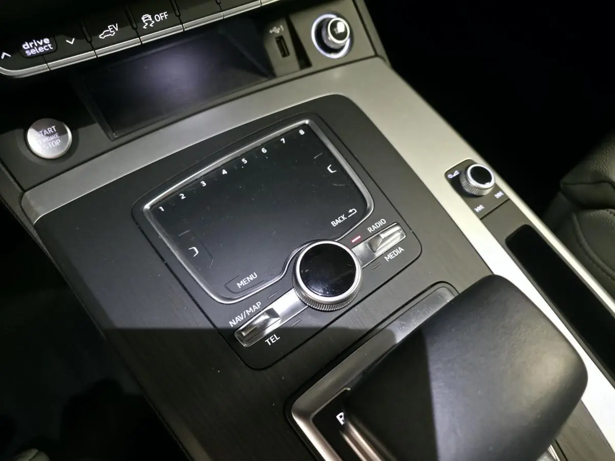 Gros plan sur la console centrale noire et grise de l'Audi Q5 S line avec commandes multimédia et bouton start/stop.