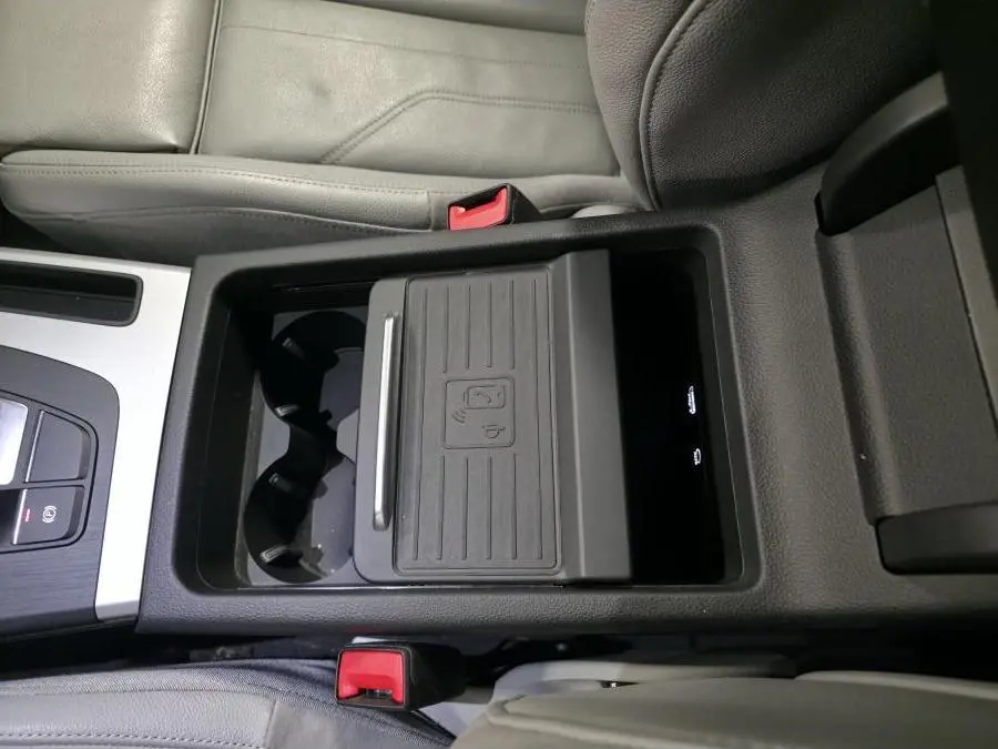 Vue plongeante sur la console centrale noire et grise de l'Audi Q5 S line 2019 avec chargeur à induction et porte-gobelets.