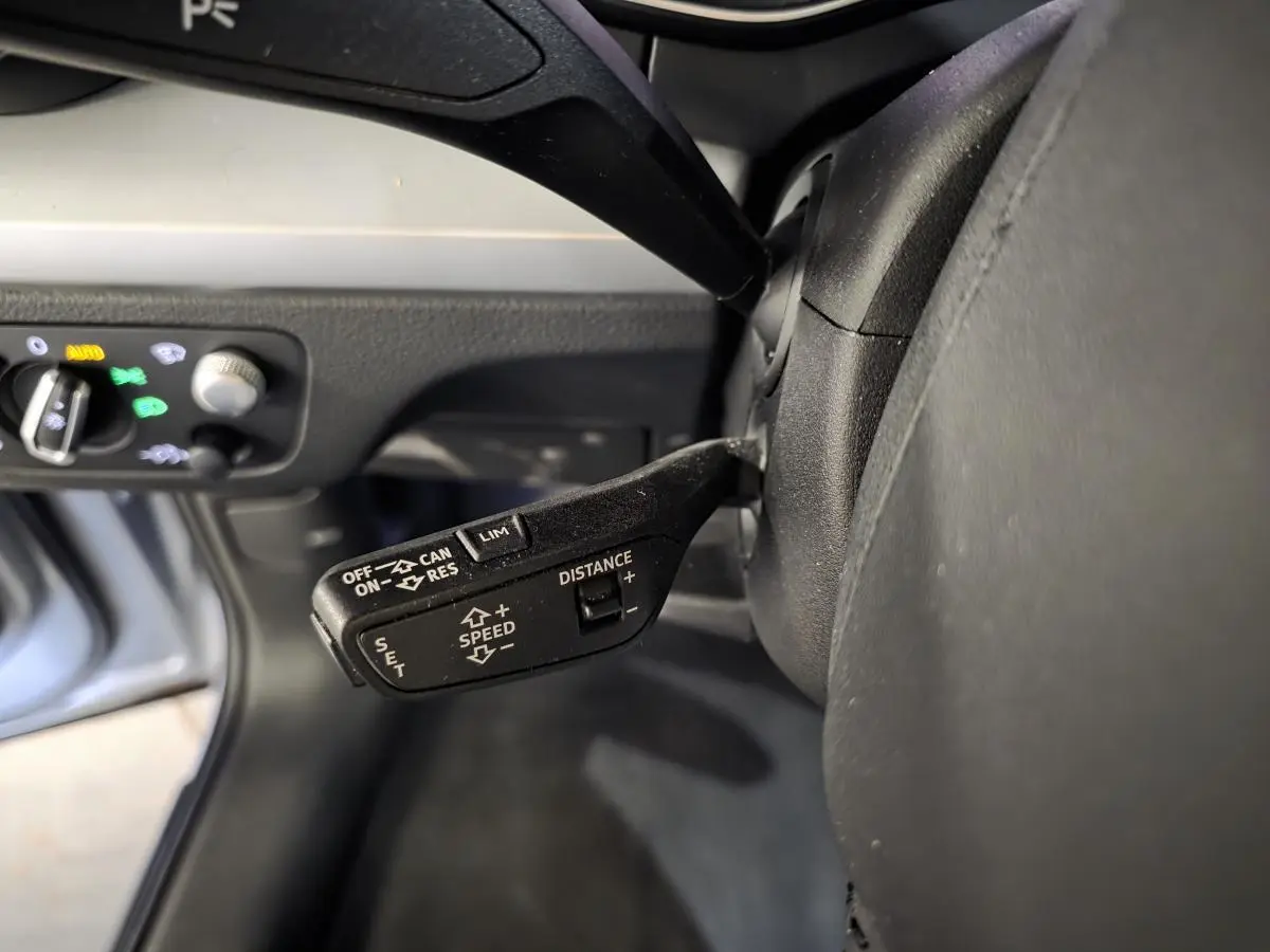Gros plan sur la commande de régulateur de vitesse adaptatif côté gauche du volant dans l’habitacle gris d’un Audi Q5 hybride rechargeable.