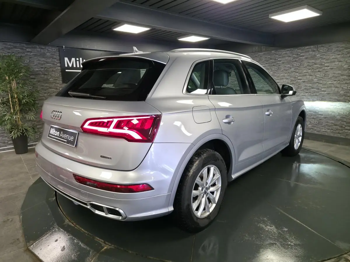 Audi Q5 hybride rechargeable gris, vue 3/4 arrière droit, feux arrière LED allumés et jantes 17 pouces.