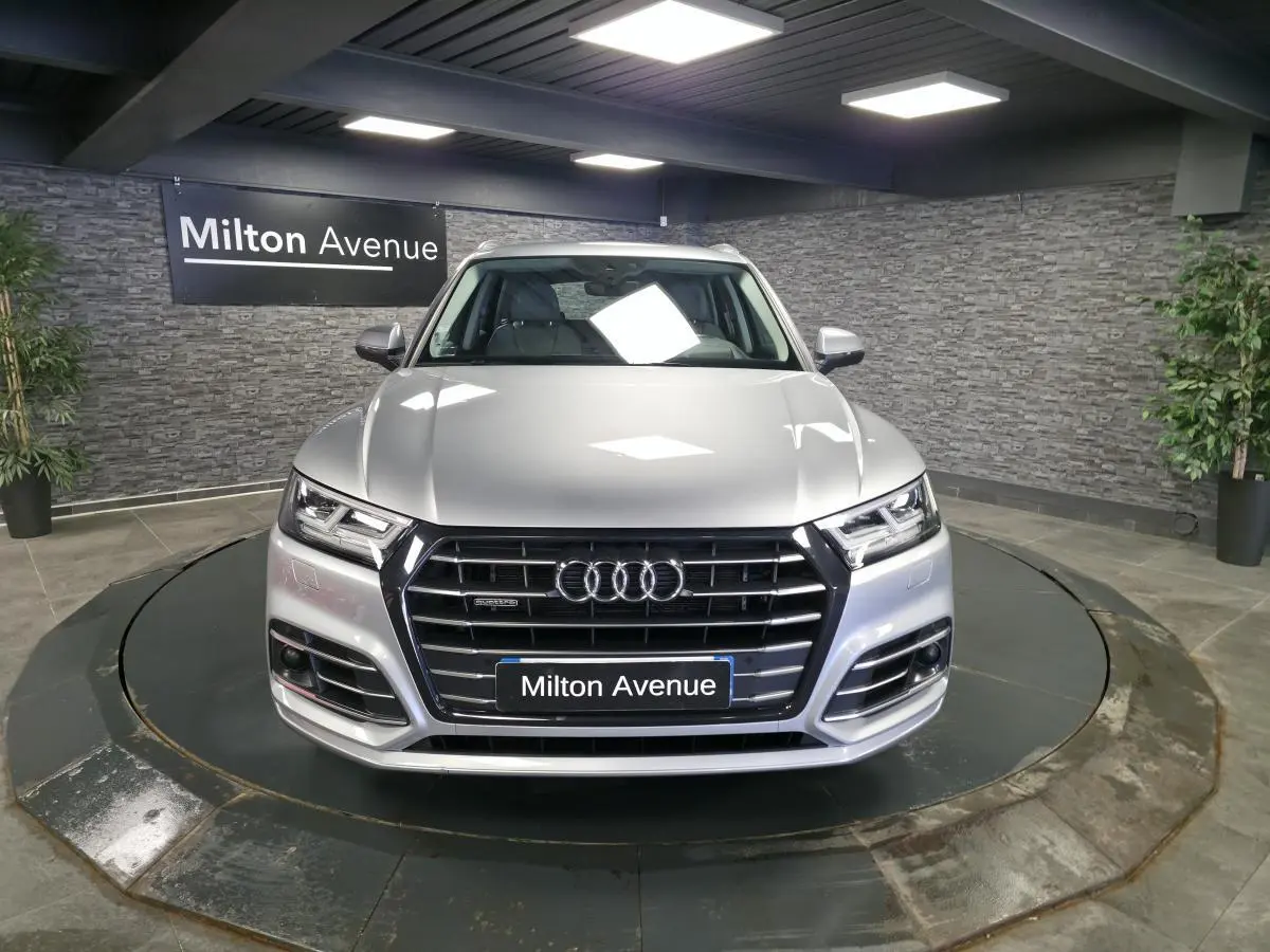 Vue frontale d'un Audi Q5 gris métallisé S line avec calandre noire et phares LED dans un showroom.