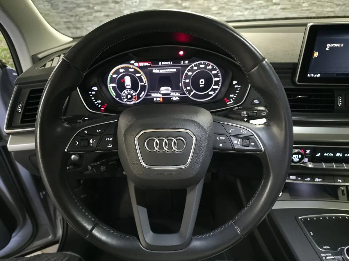 Vue centrée sur le volant cuir noir et le tableau de bord numérique de l'Audi Q5 hybride rechargeable gris de 2019.
