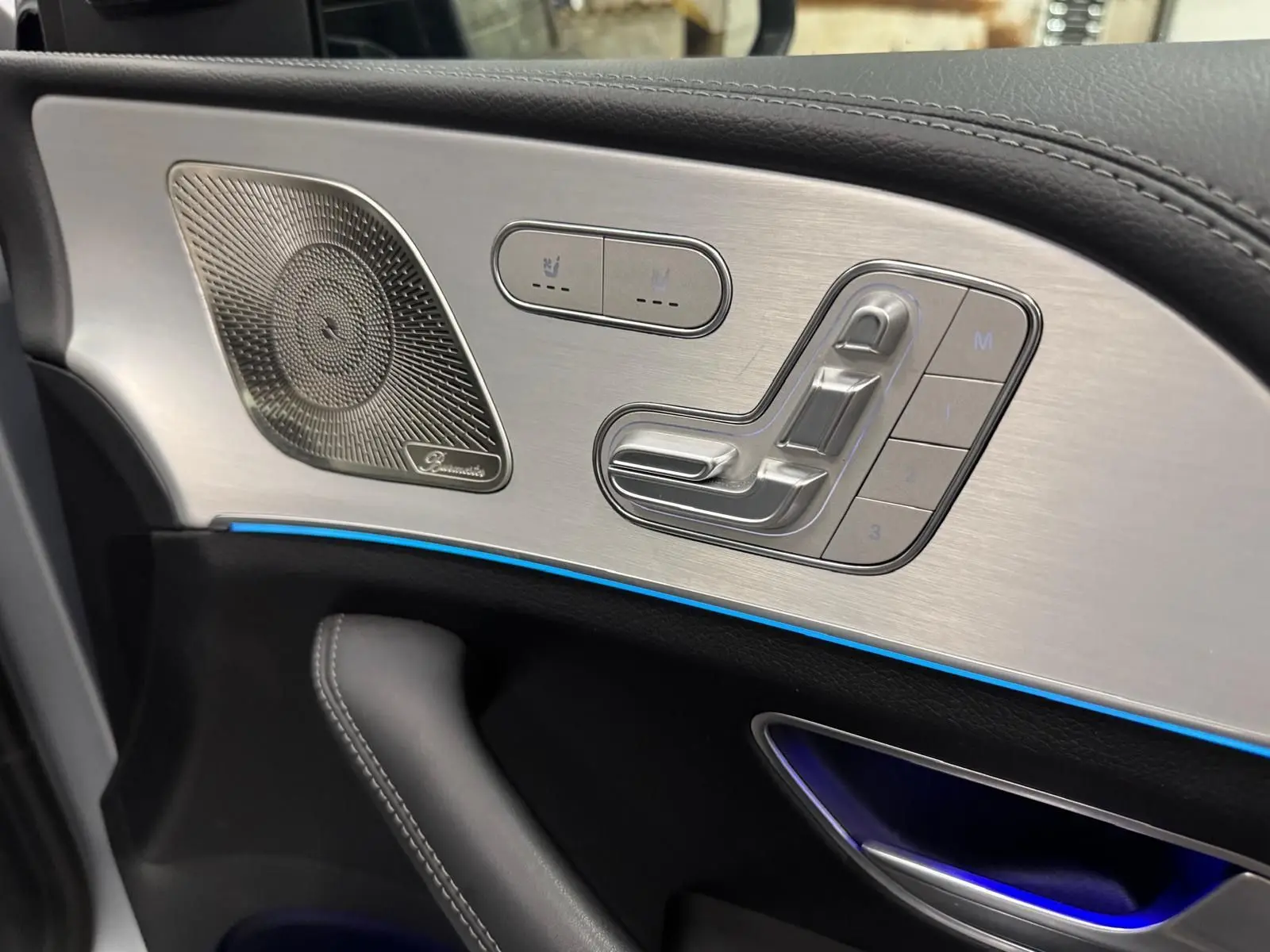 Détail de la porte côté gauche du Mercedes GLE 400 E Hybrid AMG 2023, avec commandes de siège en aluminium brossé et éclairage d’ambiance bleu.