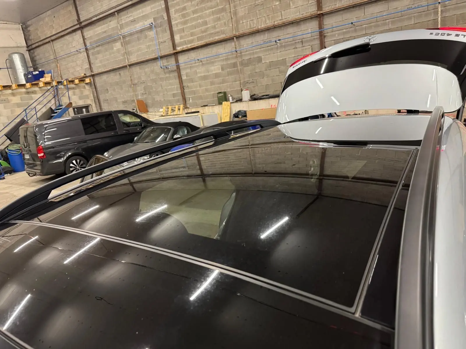 Vue rapprochée du toit panoramique noir du Mercedes GLE 400 E Hybrid argent, avec hayon arrière ouvert en intérieur.