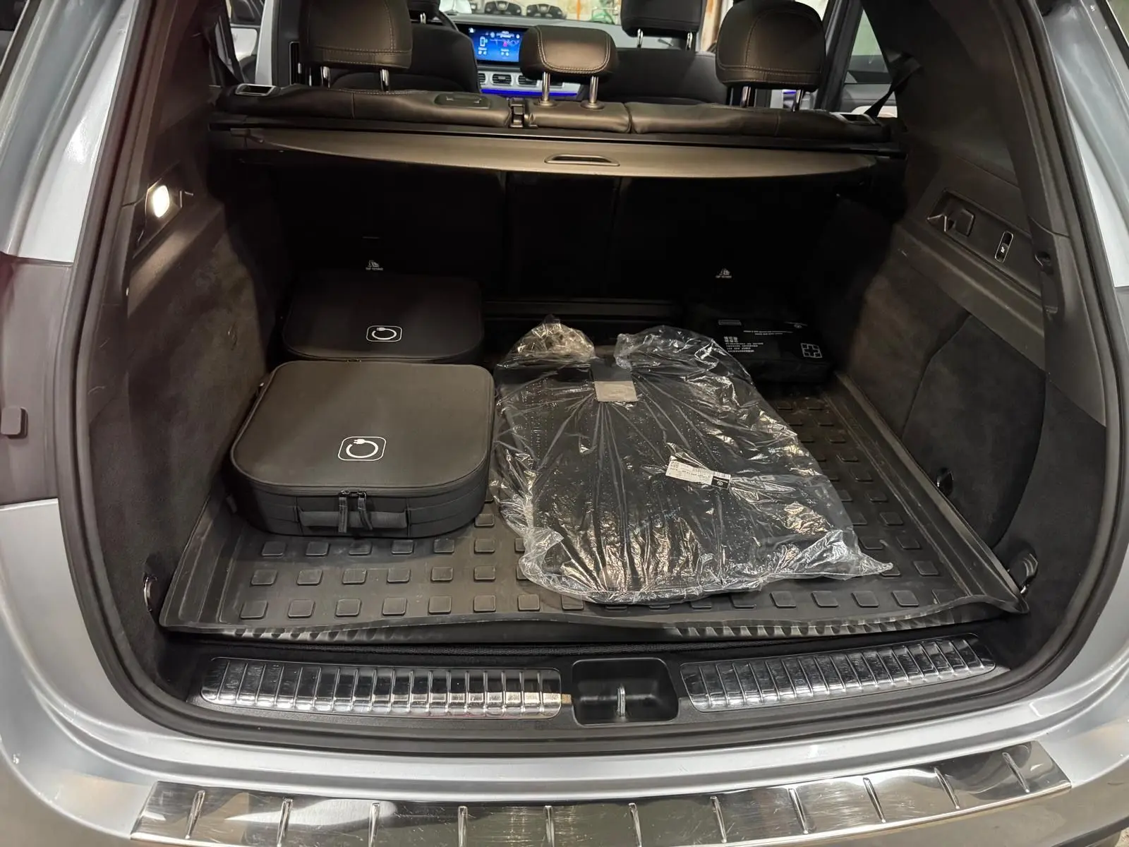 Coffre ouvert vu de l'arrière d'un Mercedes GLE 400 E Hybrid argent métallisé avec tapis et accessoires rangés.