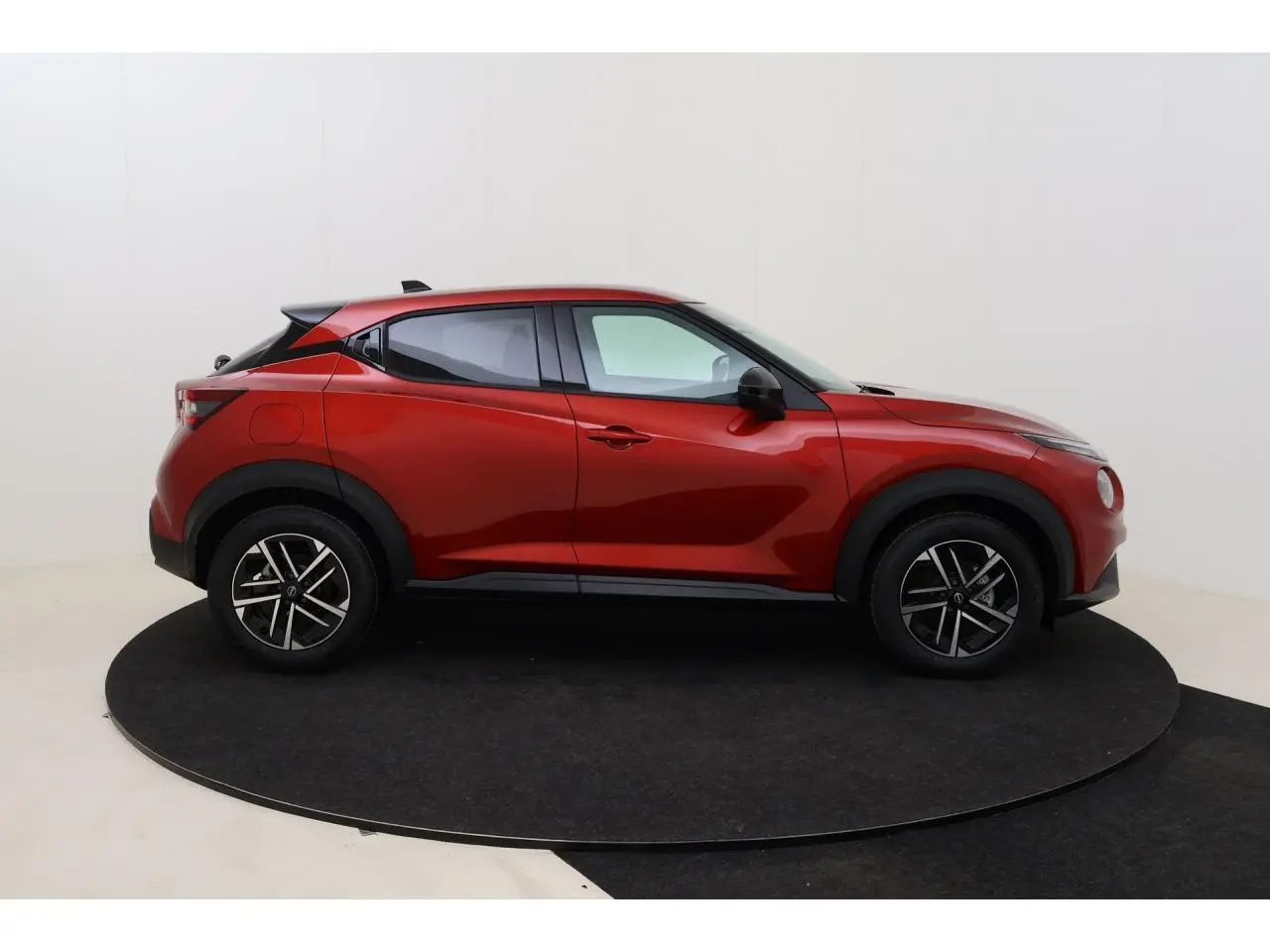 Vue de profil côté gauche d'un Nissan Juke 2026 rouge Fuji Sunset avec jantes alliage 17 pouces et toit noir.