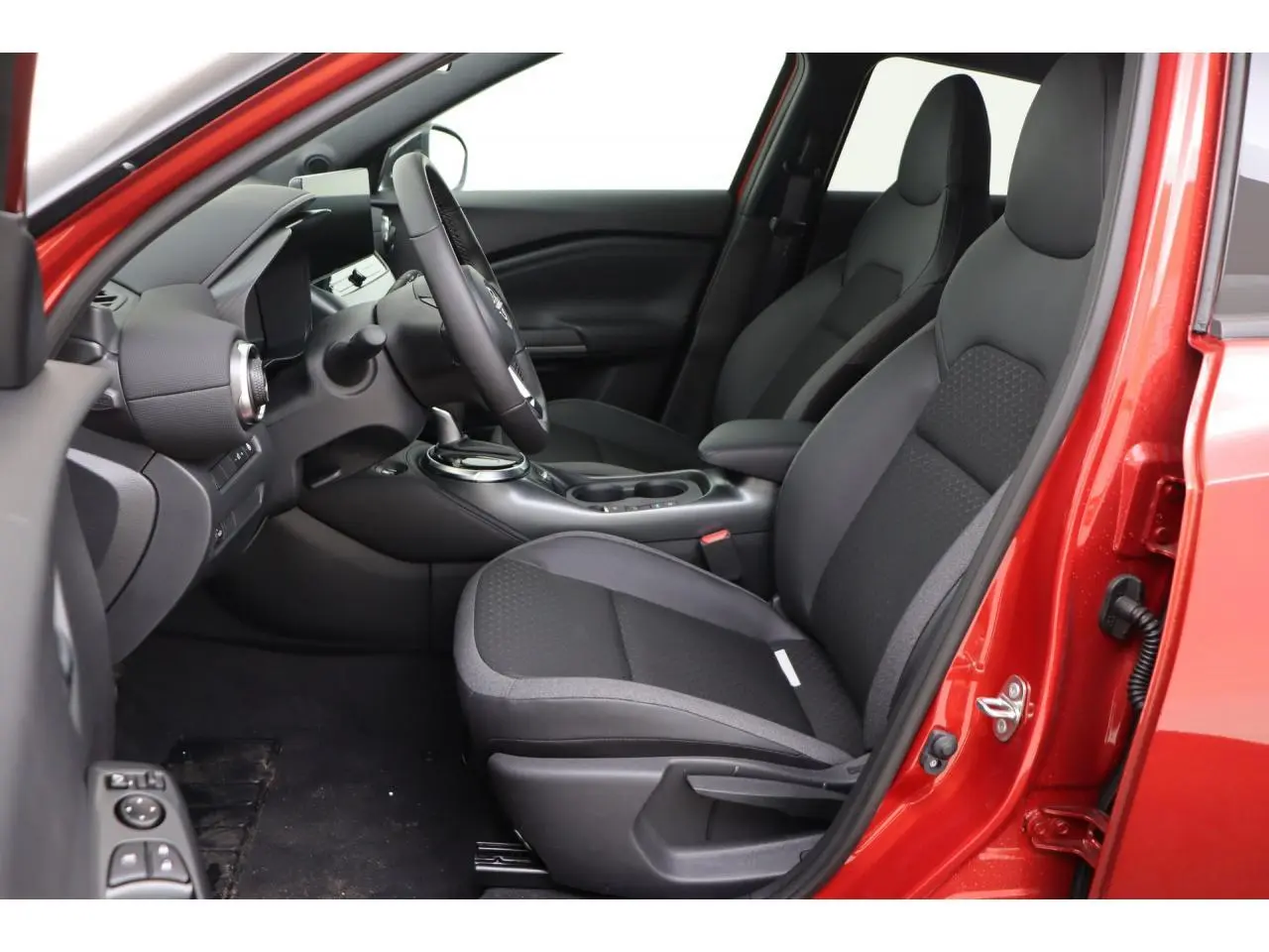 Vue intérieure côté conducteur du Nissan Juke rouge Fuji Sunset 2026, montrant sièges noirs et tableau de bord moderne.