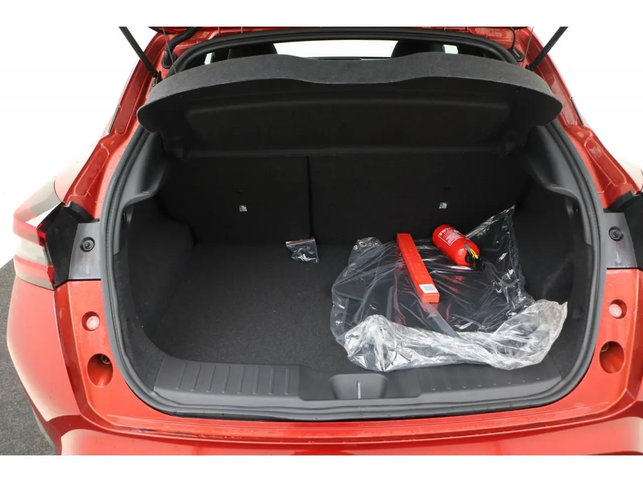 Coffre ouvert d’un Nissan Juke rouge Fuji Sunset, montrant un espace de rangement avec extincteur et triangle de signalisation.