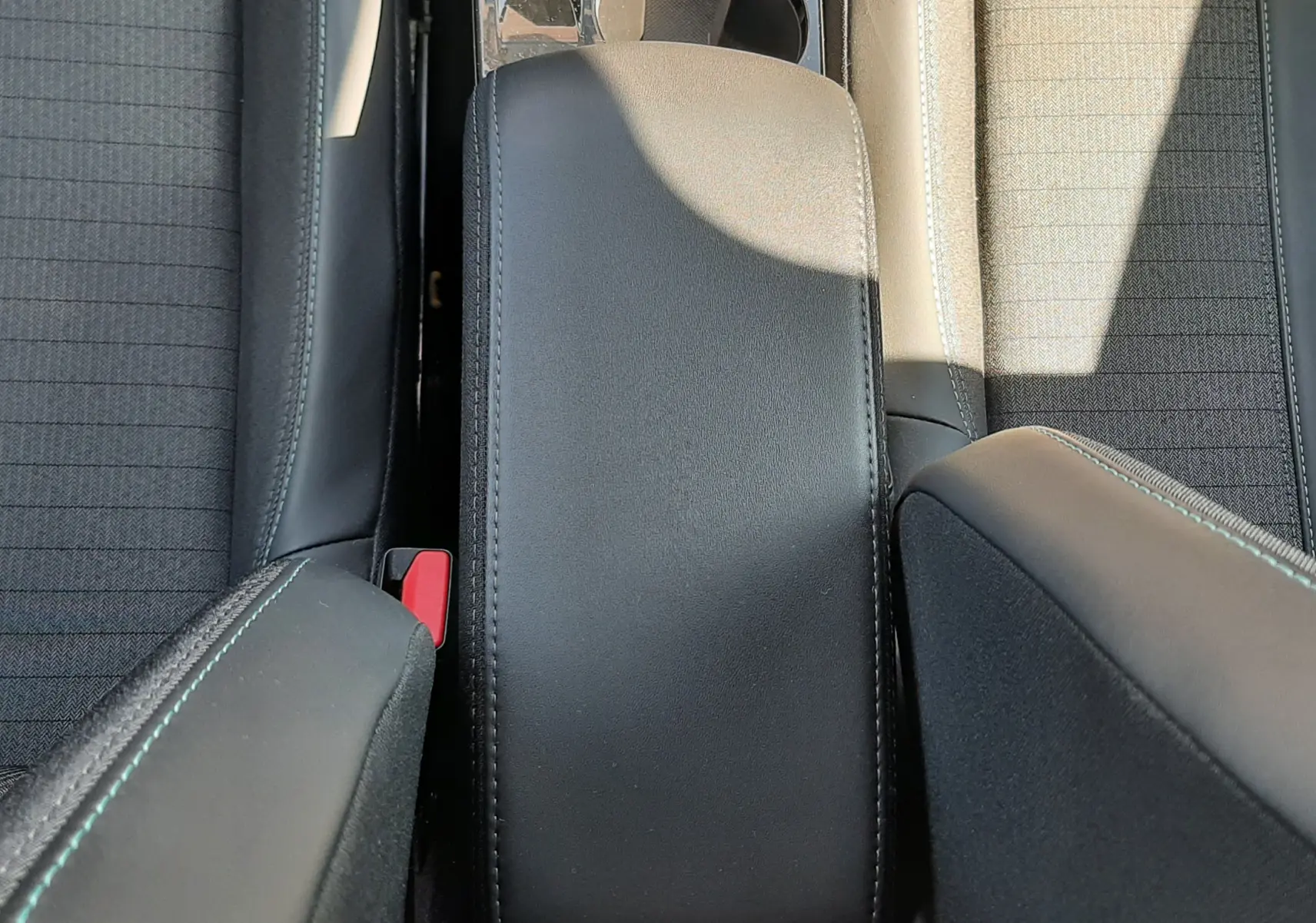 Vue plongeante sur l'accoudoir central noir et les sièges tissu gris du Peugeot 2008 1.5 BlueHDi 2023.