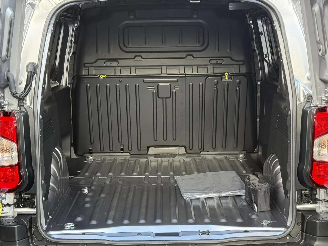 Vue arrière ouverte du Citroën Berlingo gris Artense montrant l'espace de chargement tôlé et vide avec deux petits objets au sol.