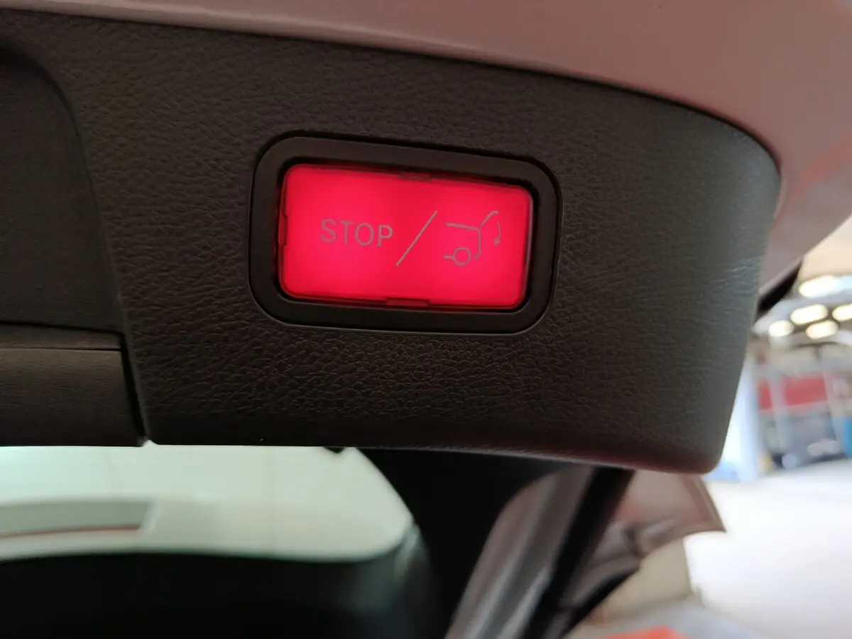 Gros plan sur le bouton rouge stop d'ouverture électrique du coffre du Mercedes GLA gris clair, vue intérieure arrière.