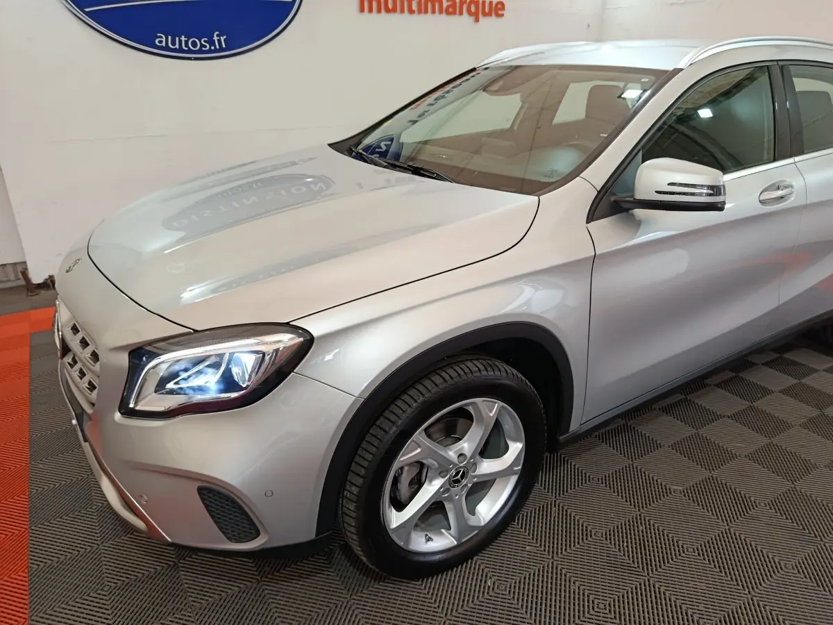 Vue 3/4 avant droit d'une Mercedes GLA 200 d Business Executive gris clair avec phares LED allumés et jantes alliage.