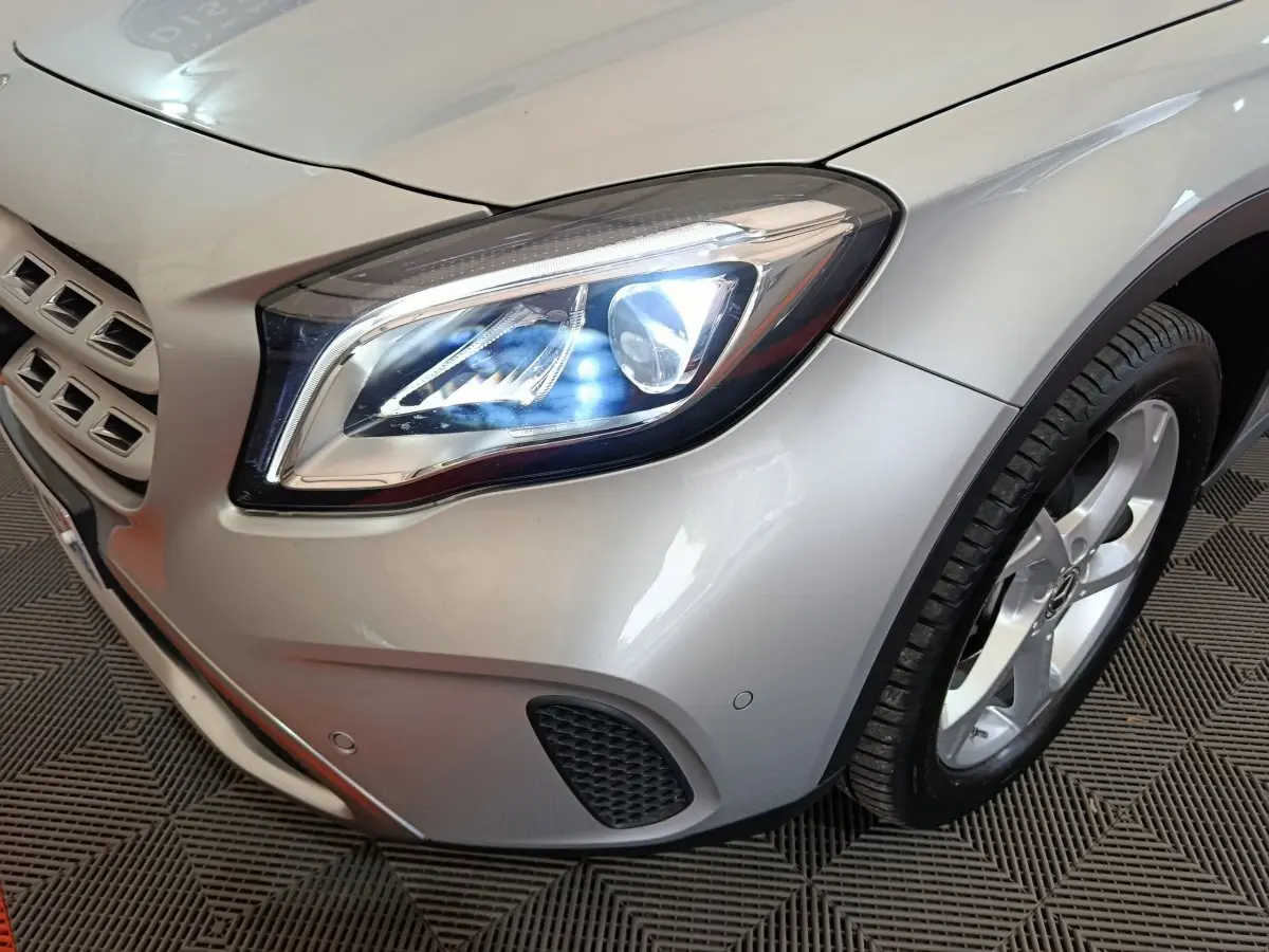Gros plan sur l'avant droit gris clair d'une Mercedes GLA 200 d avec phares LED allumés et jante alliage visible.