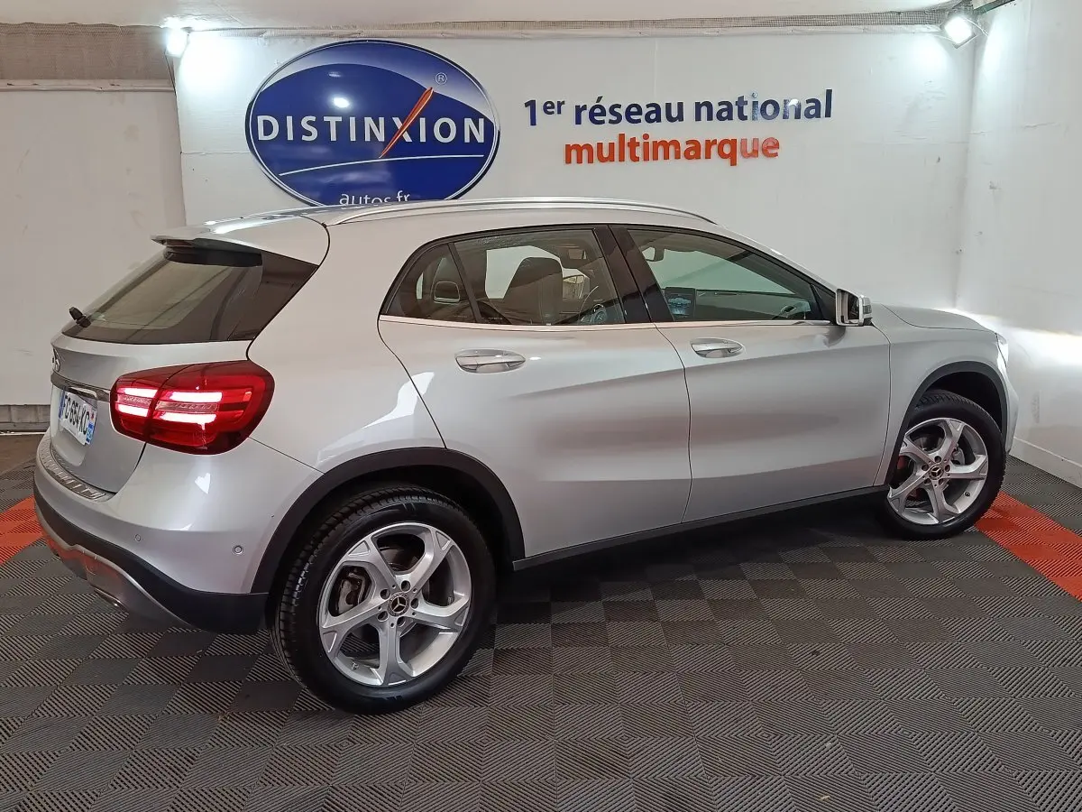 Vue latérale côté droit d'un Mercedes GLA 200 d gris clair 2018 avec jantes alliage et feux arrière allumés en intérieur showroom.
