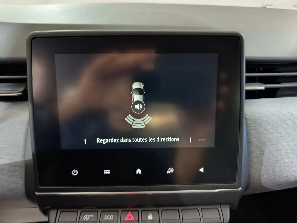Écran tactile central de la Renault Clio gris clair 2025 affichant une alerte de surveillance des alentours.