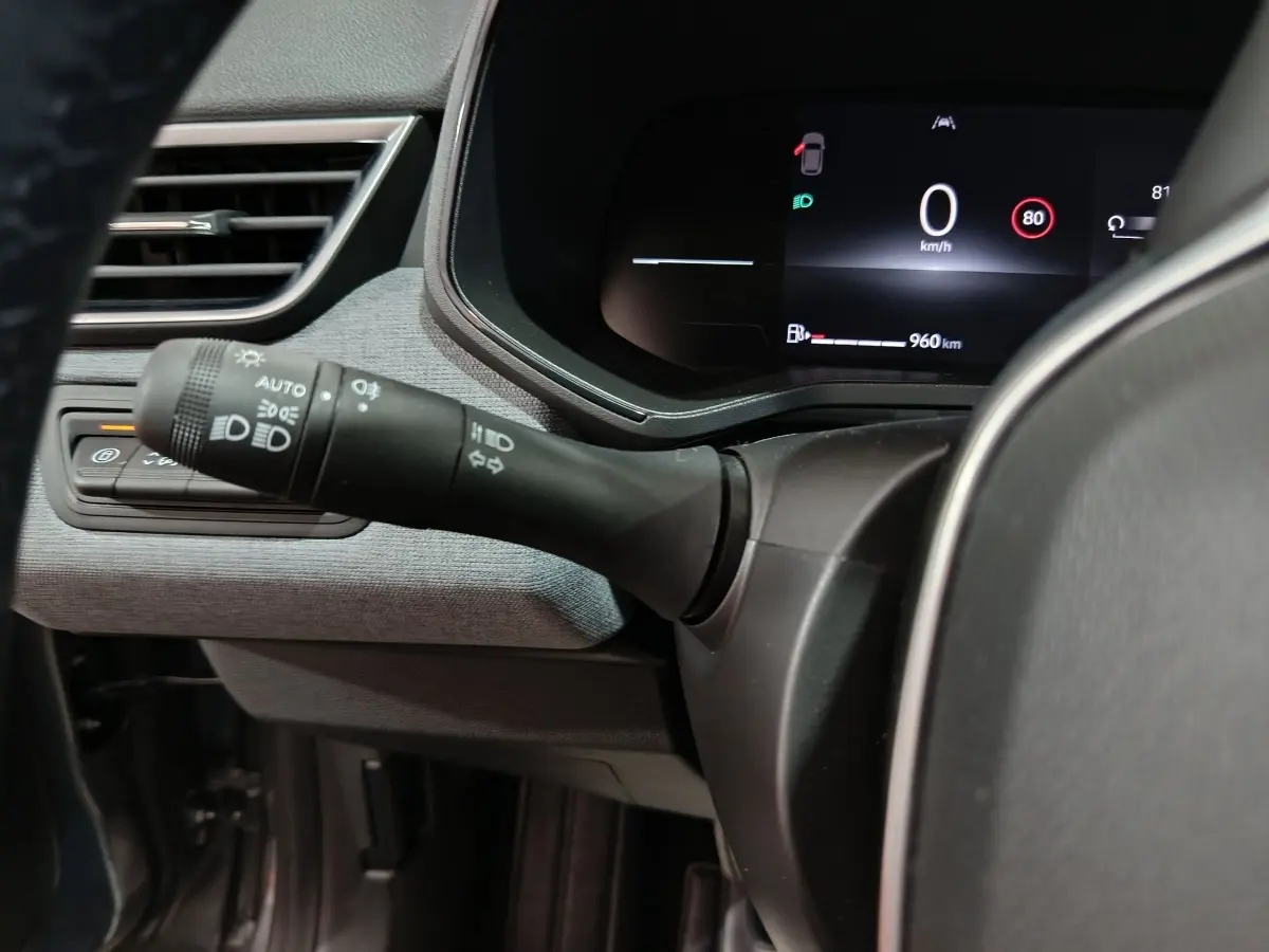 Vue rapprochée du combiné d'instruments numérique et du commodo des phares dans le tableau de bord gris clair de la Renault Clio 2025.