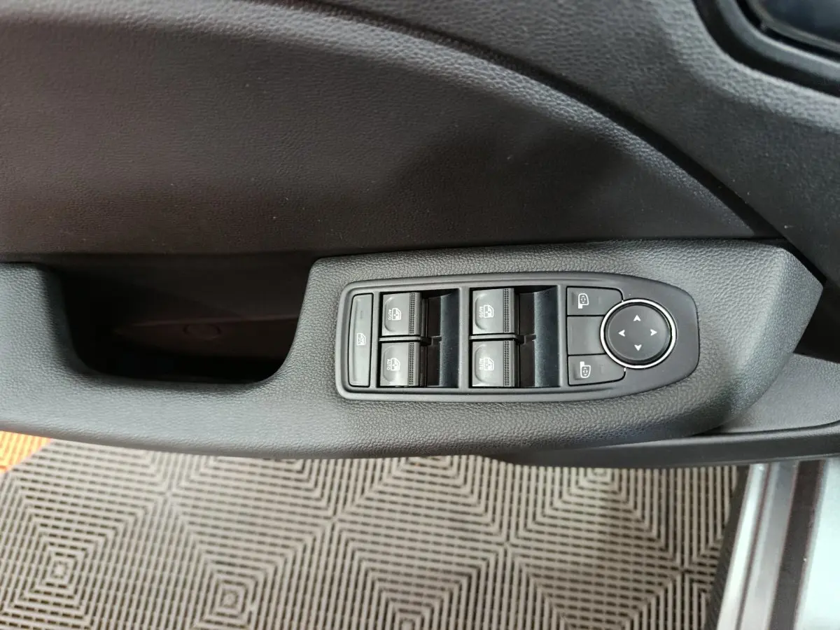 Gros plan sur les commandes des vitres électriques et rétroviseurs côté gauche d'une Renault Clio gris clair 2025.