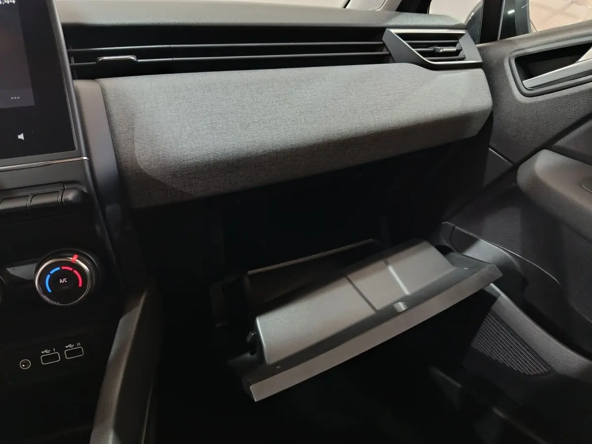 Vue intérieure côté passager de la Renault Clio gris clair 2025, avec boîte à gants ouverte et commandes de climatisation visibles.