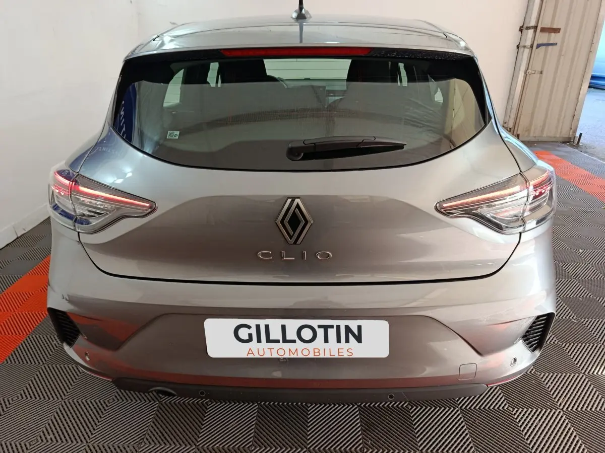 Vue arrière d'une Renault Clio gris clair 2025 avec feux LED et logo Renault bien visibles dans un garage.