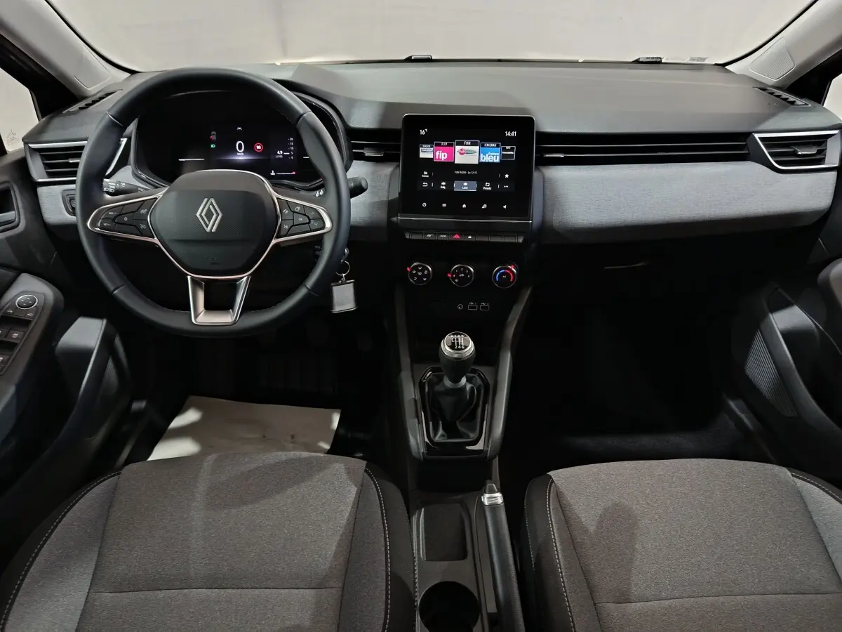 Vue intérieure frontale du tableau de bord de la Renault Clio gris clair 2025 avec écran tactile et volant multifonctions.