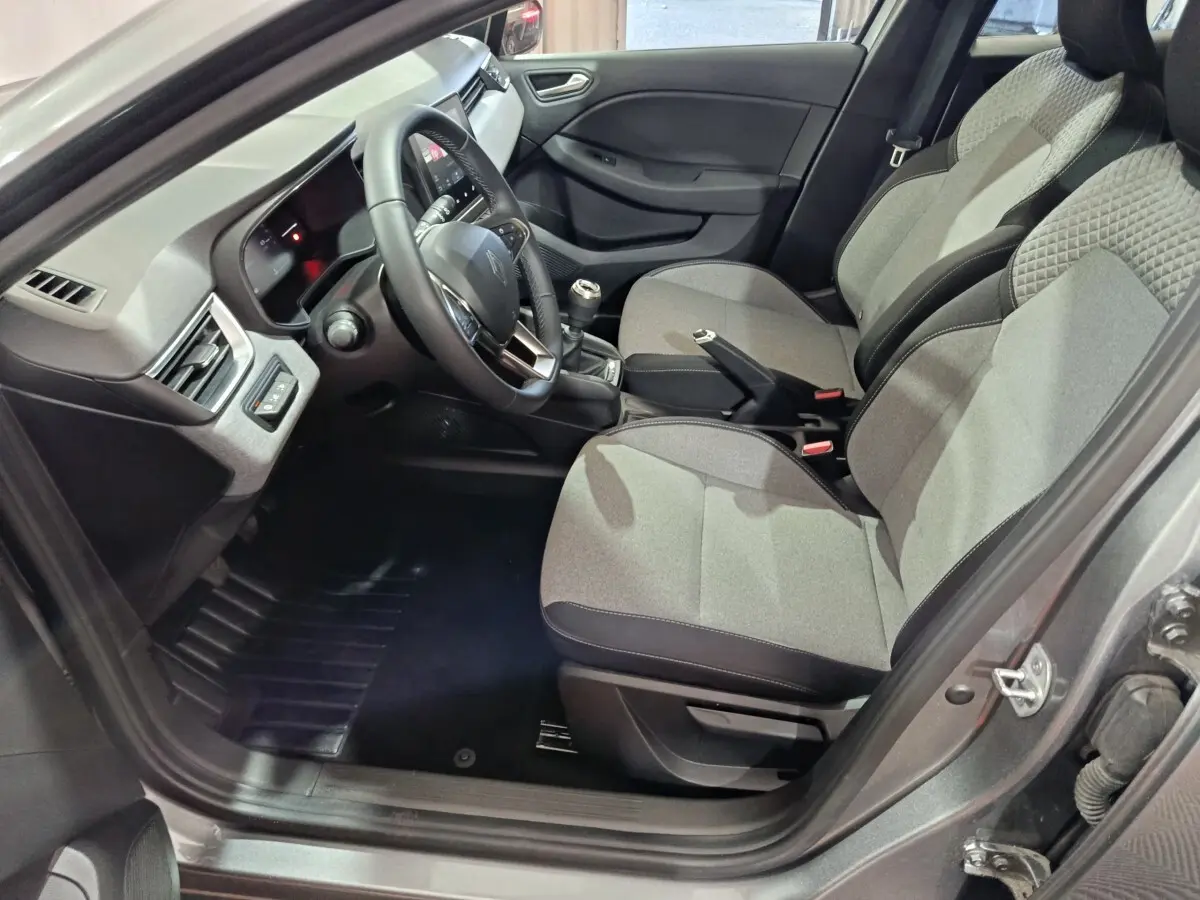 Vue intérieure côté conducteur de la Renault Clio gris clair 2025, montrant sièges tissu et tableau de bord moderne.