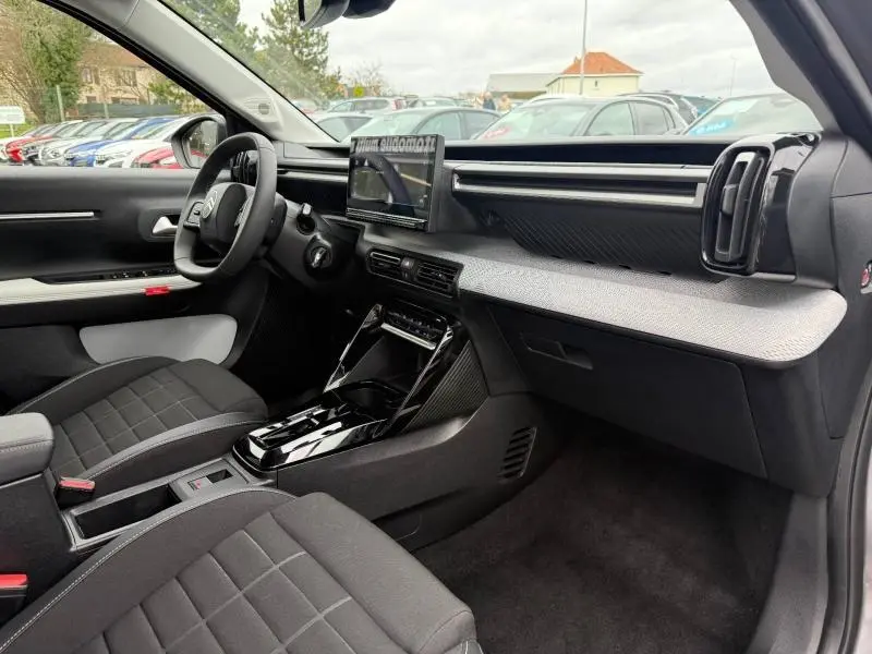 Vue intérieure côté conducteur de la Citroën C3 électrique 2025 avec tableau de bord gris clair et sièges noirs.