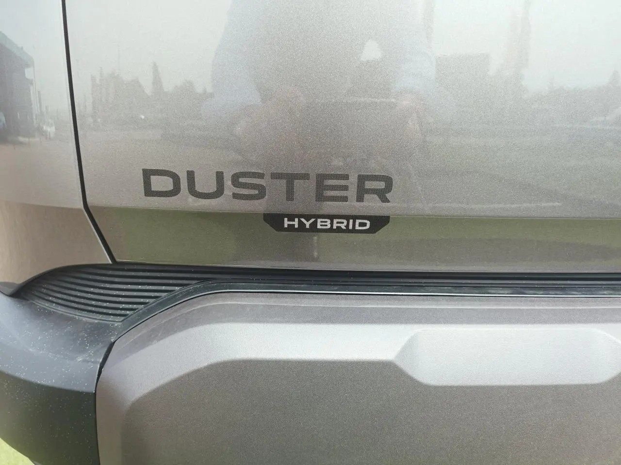 Gros plan sur le logo Duster et l’inscription Hybrid sur la partie arrière gris schiste métallique du SUV Dacia Duster.