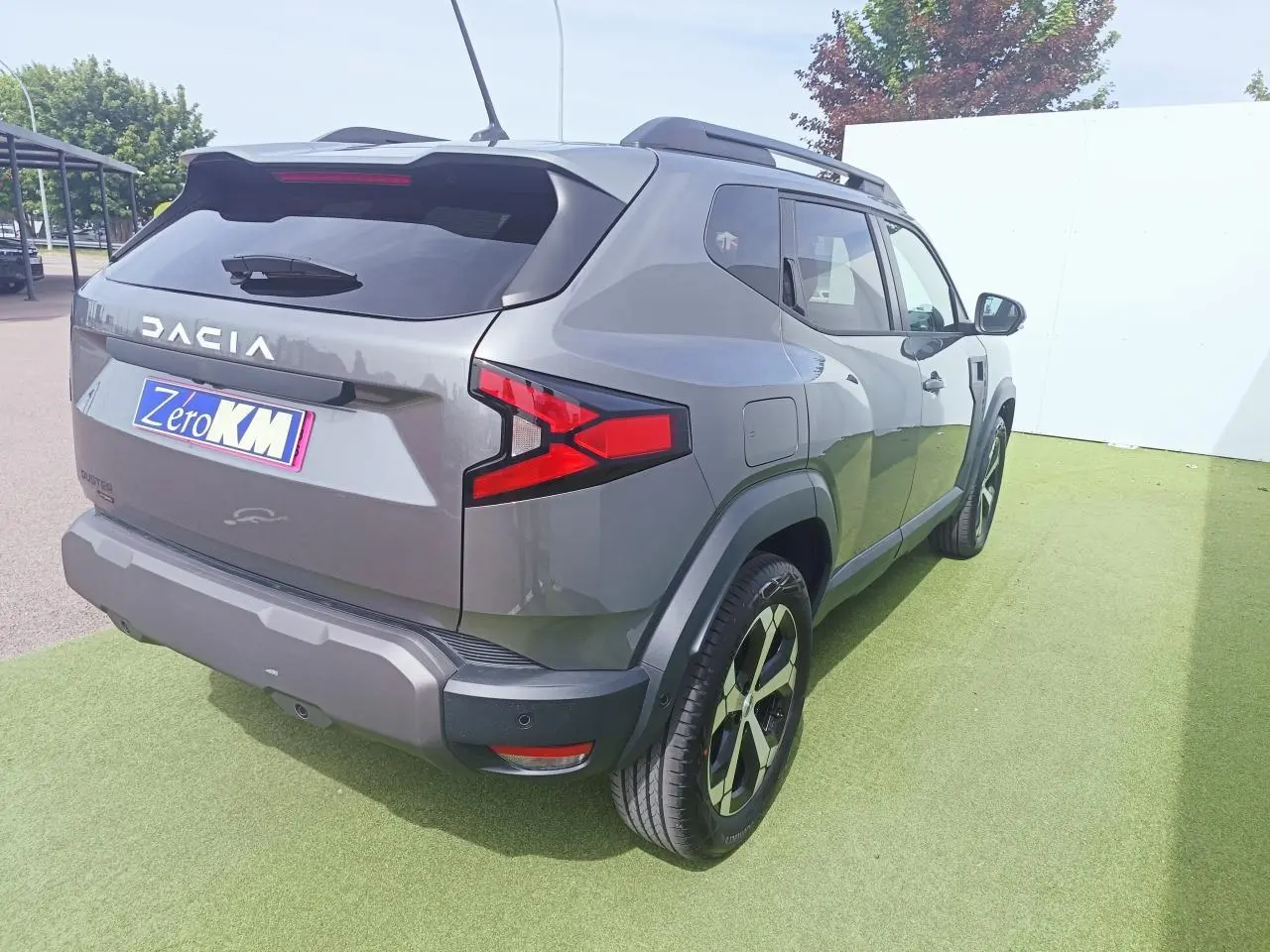 Vue 3/4 arrière droite du Dacia Duster gris schiste métallisé avec jantes alliage diamantées et barres de toit noires.