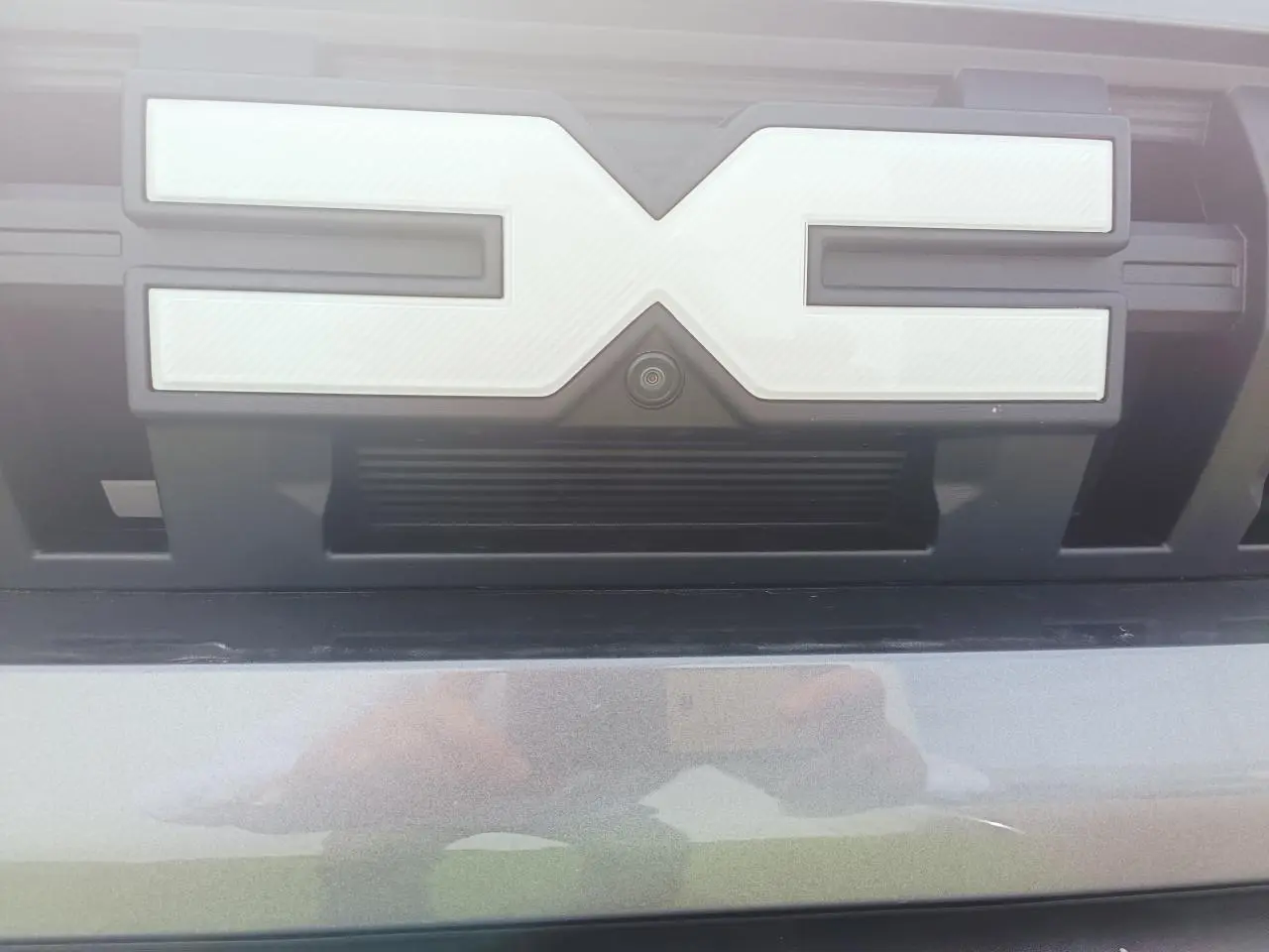 Gros plan sur la calandre avant gris schiste métallisé du Dacia Duster III avec caméra intégrée sous le logo.