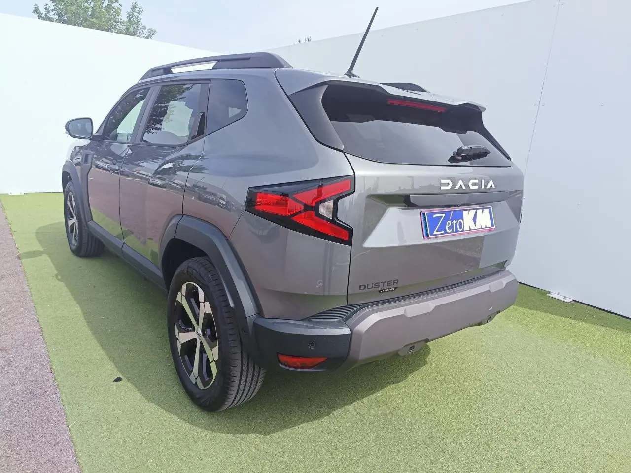Vue 3/4 arrière droite du Dacia Duster III gris schiste métal avec jantes alliage et barres de toit noires.